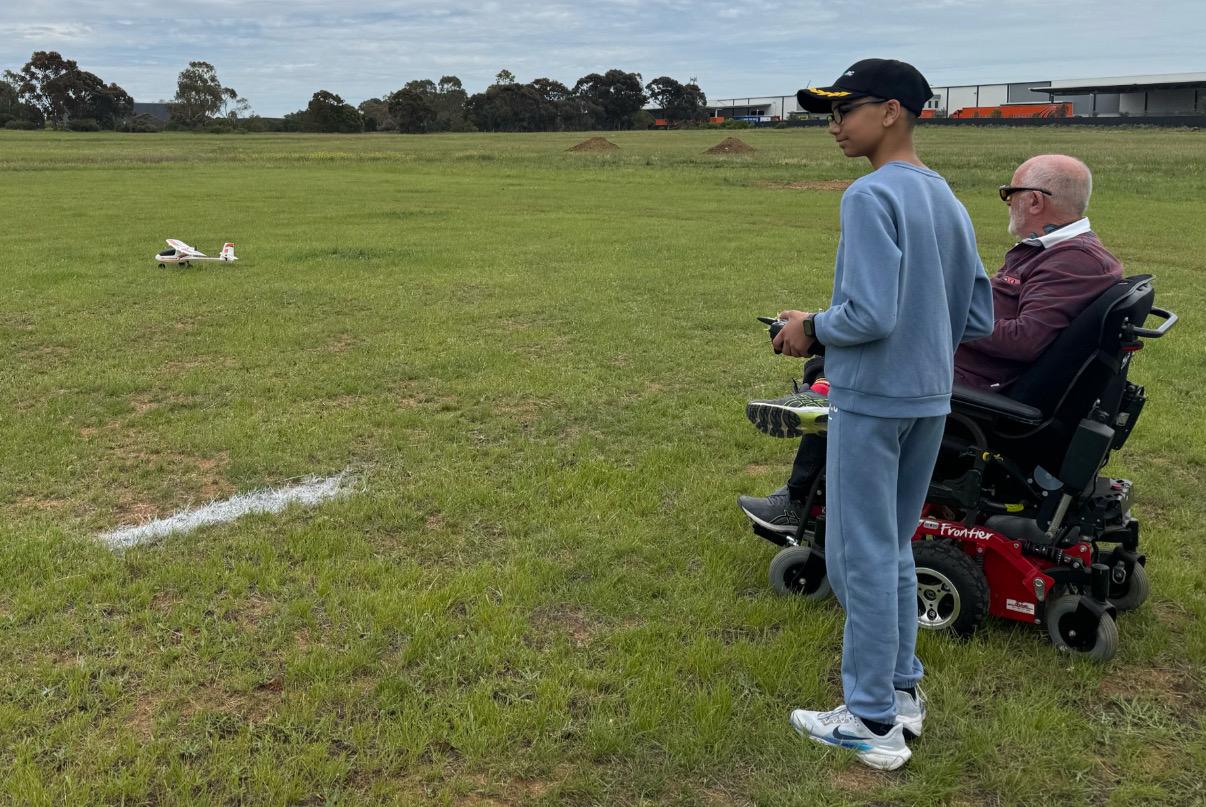 A young pilot flying a fixed-wing model alongside a member in a wheelchair