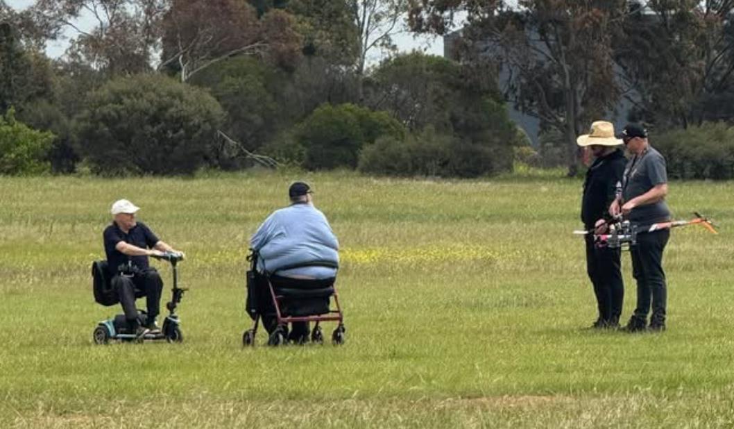 Members on mobility scooters watching a helicopter fly